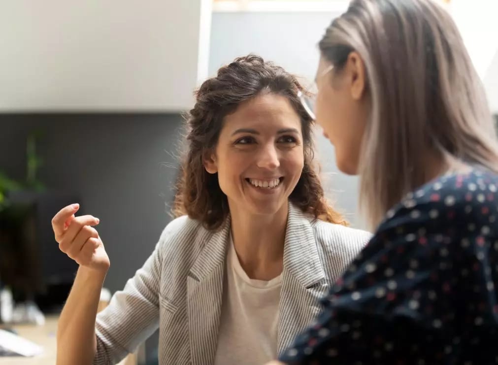 Two women conversing, one smiling warmly.