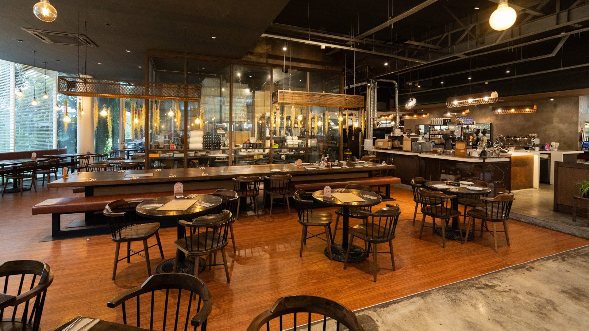 A spacious modern restaurant with wooden tables, industrial lighting, large windows, and a bar.