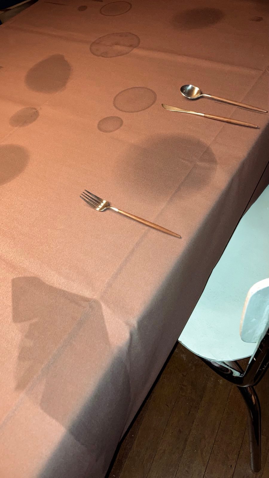 Brown tablecloth with numerous water rings, a fork, knife, and spoon laid out.
