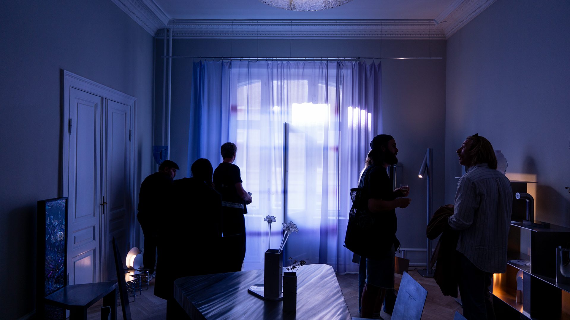 Silhouetted people in a blue-lit room with large windows.