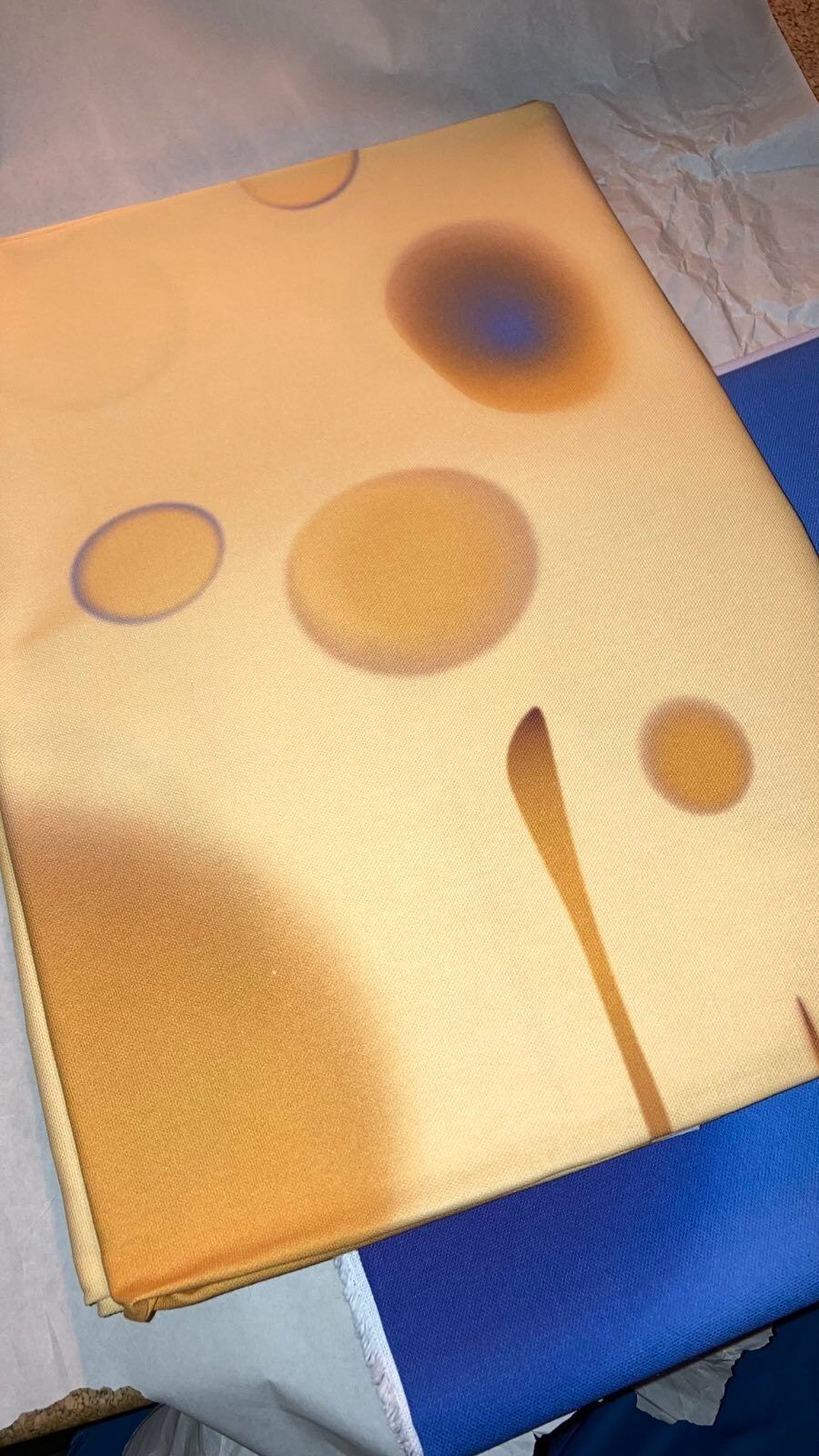 Yellow fabric with abstract brown and blue spots, partially covering blue fabric.