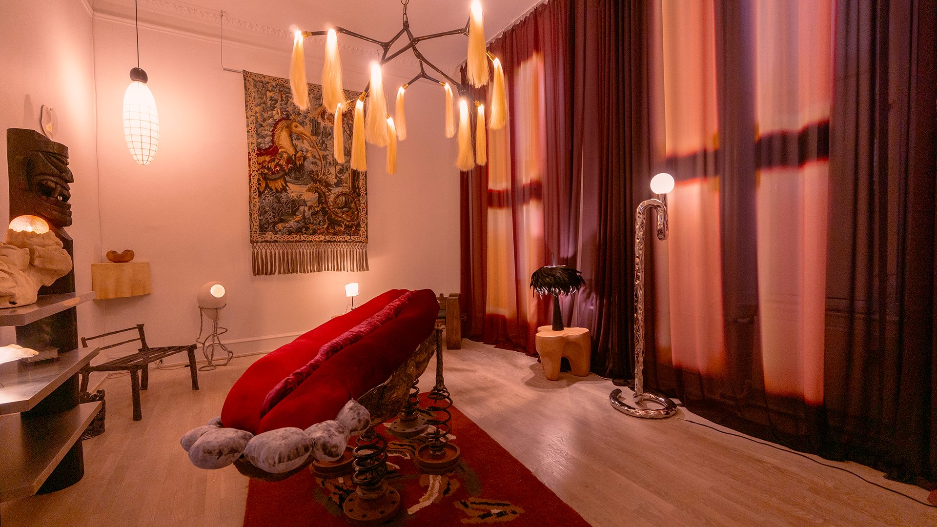 Eclectic room with red lip sofa, hair chandelier, tapestry, and unique art objects.