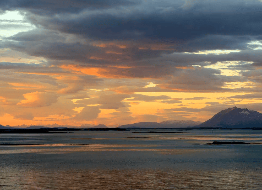 Vibrant sunset sky with orange clouds reflecting on calm waters, framed by distant mountains.