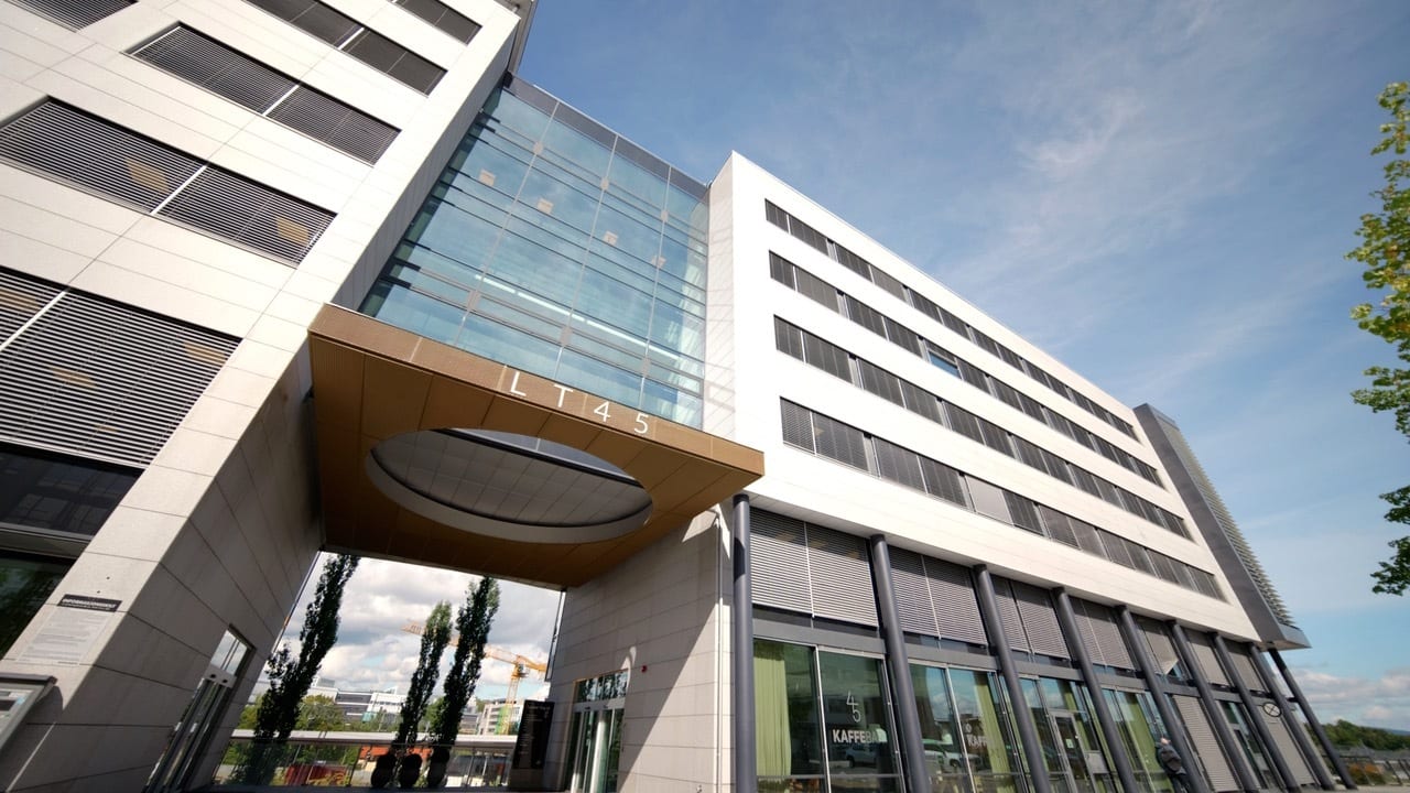 Modern office building with white facades, glass sections, and a distinctive arched entrance under a blue sky.