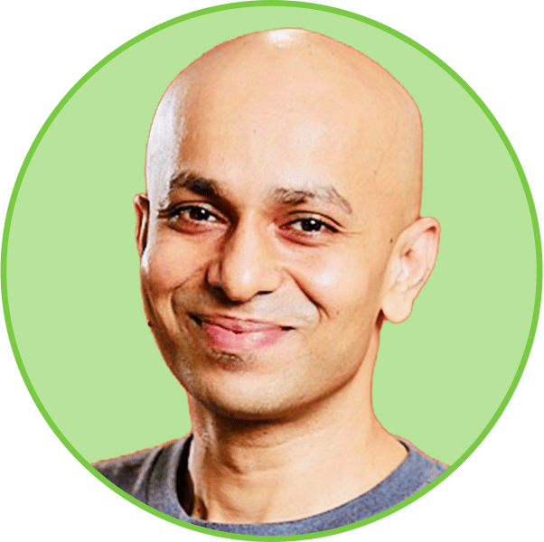 Smiling bald man with dark eyes in a gray t-shirt against a light green circular background.