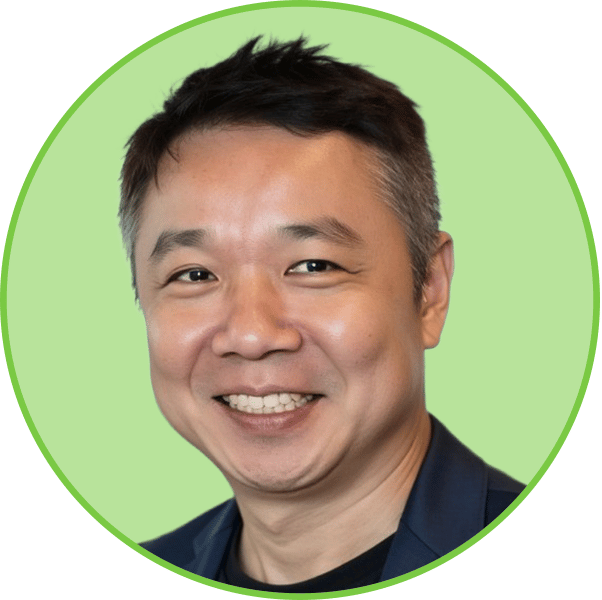 A headshot of a smiling East Asian man in a dark jacket, set against a light green background.