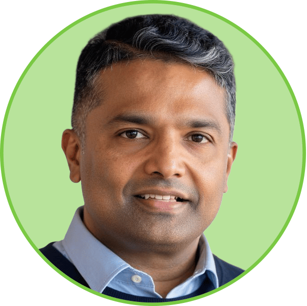 Headshot of a smiling man in a light blue shirt and dark sweater, looking at the camera.
