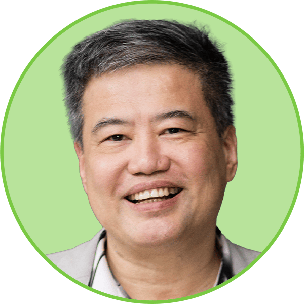 Smiling middle-aged Asian man with grey hair in a light shirt, looking at the camera.