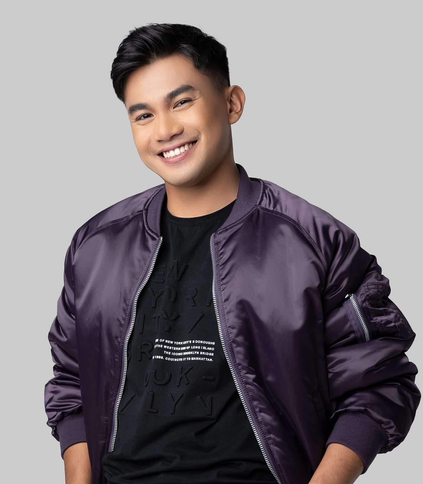 Smiling man in purple bomber jacket and black t-shirt.