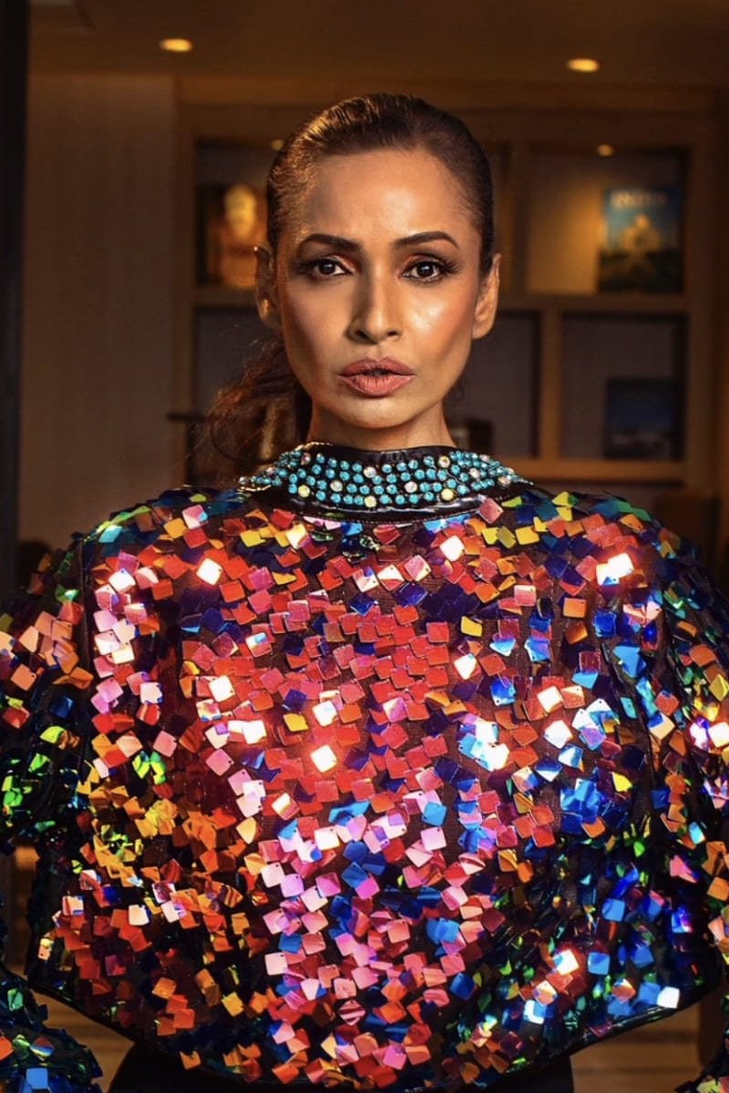 Woman with an intense gaze, in a vibrant, multi-colored square-sequined top and beaded collar.