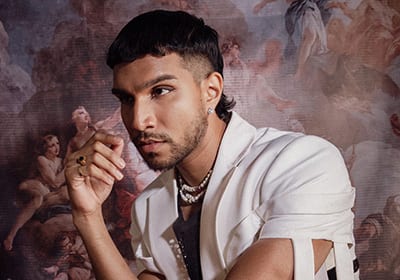 Young man with modern mullet, white jacket, and pearls, looking left against classical art.