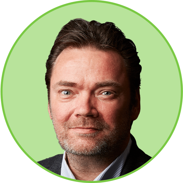 Headshot of a man with dark hair, beard, and blue eyes, smiling slightly against a green background.