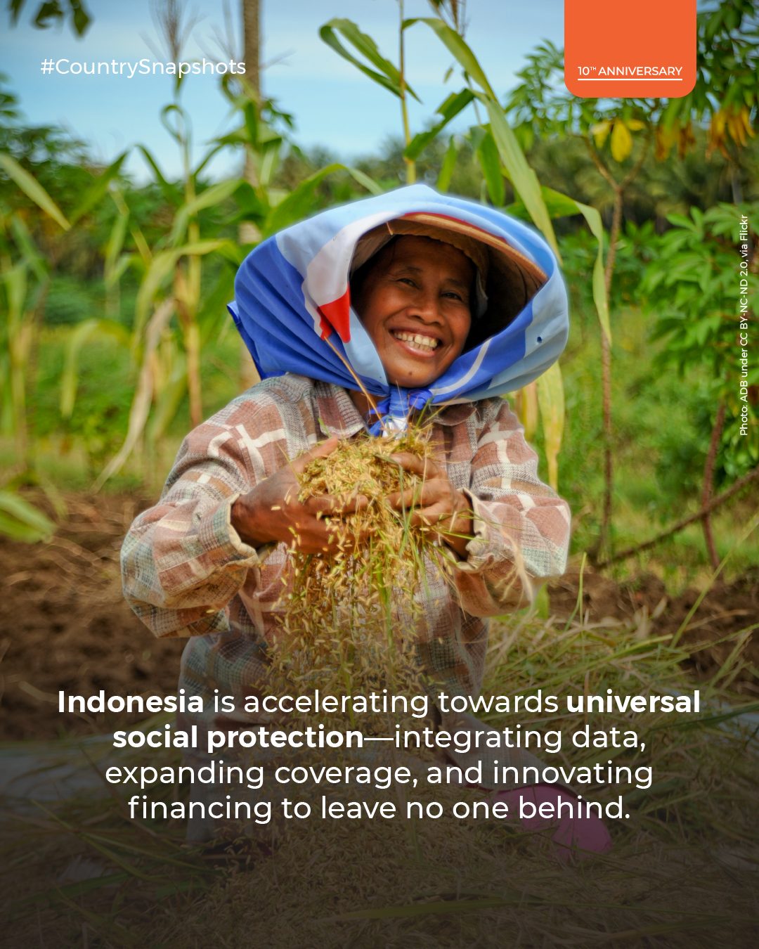 Smiling woman farmer in a field, wearing a hat, holding harvested grains.