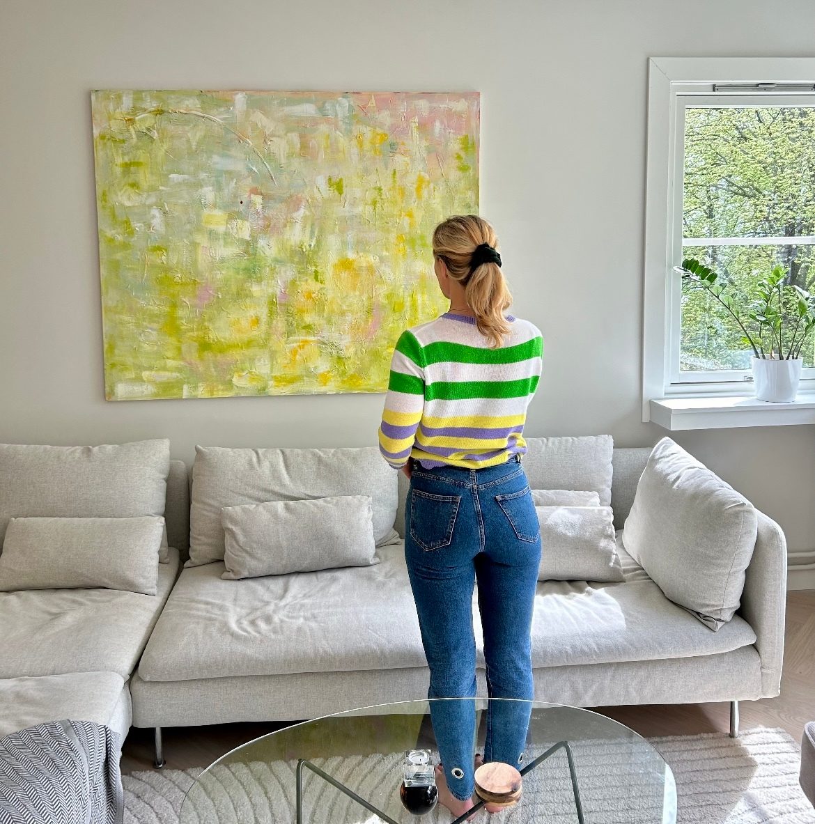 Woman in striped sweater and jeans looks at abstract painting in a living room.