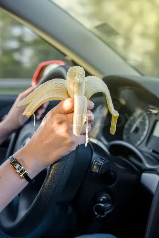 Hands on steering wheel holding a peeled banana while driving.