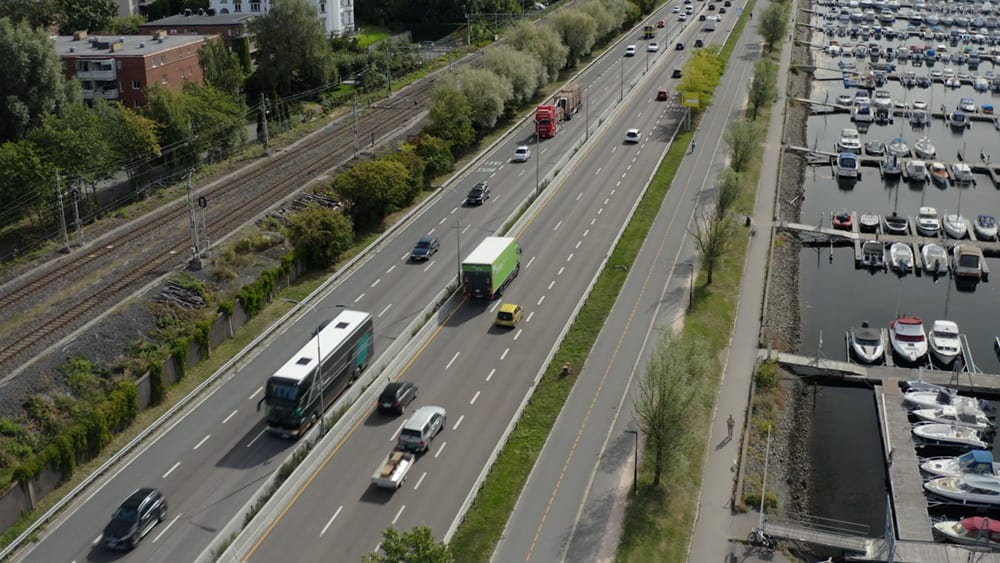 Aerial view of a highway with traffic, parallel train tracks, and a marina full of boats.