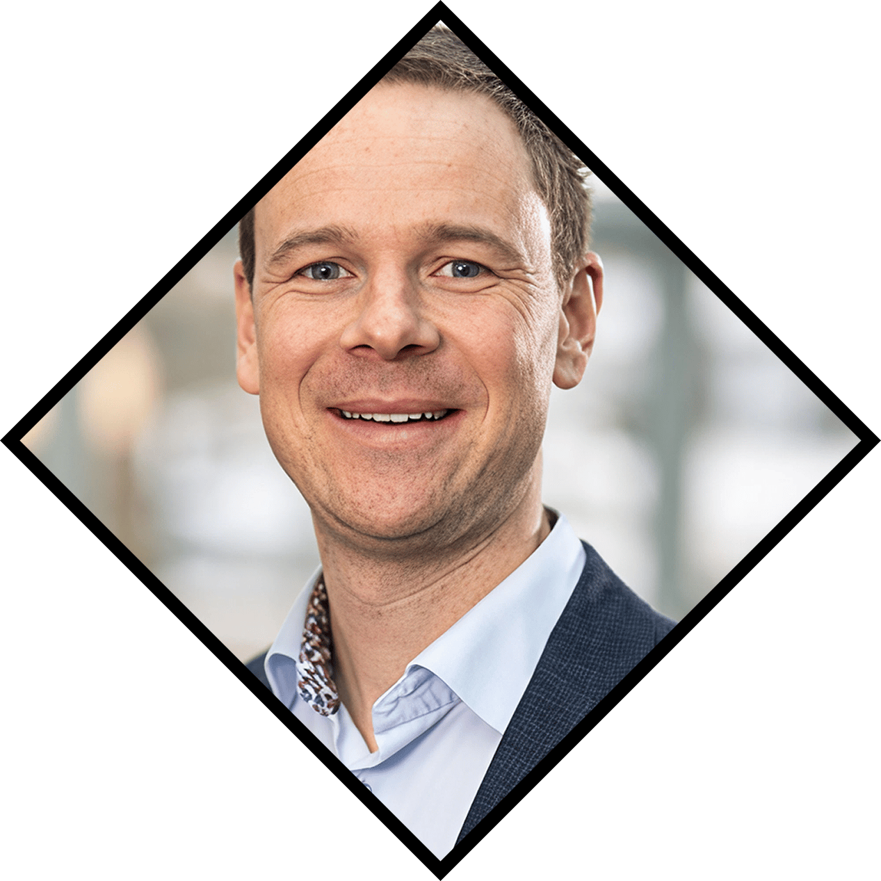 Smiling man in a blue shirt and dark suit jacket.