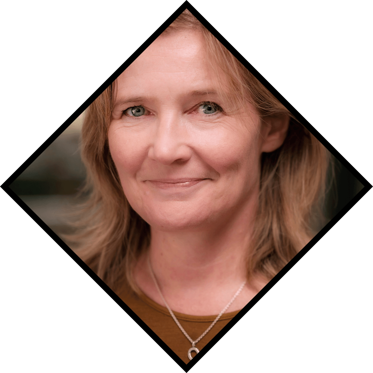 Smiling blonde woman with blue eyes and a horseshoe necklace.