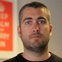 Man with short hair and stubble, facing forward with a neutral expression.