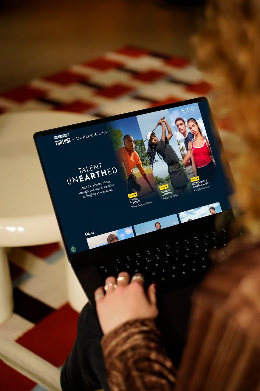 Person viewing a laptop showing "Talent Unearthed" content by Fortune + De Beers, featuring athletes.