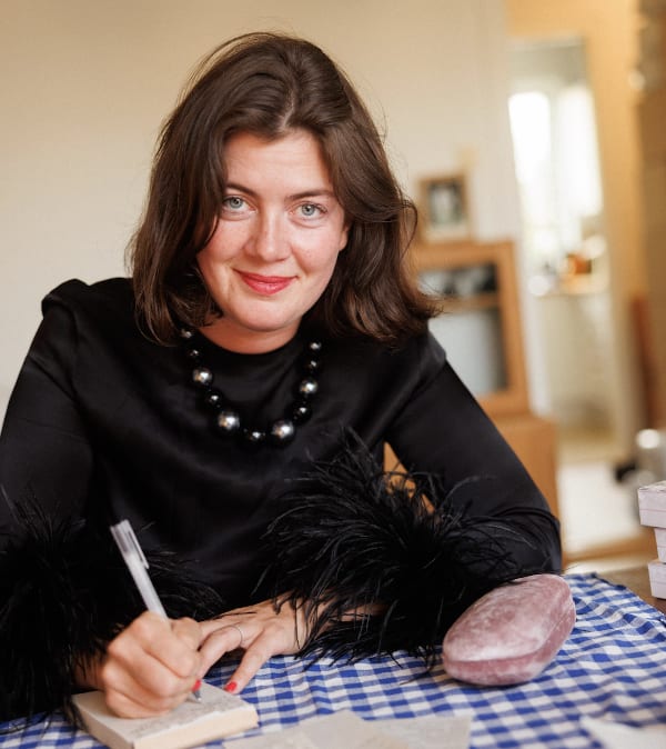 Woman in black dress with feather cuffs writing at a blue checkered table.