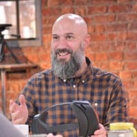 Smiling bald bearded man in a plaid shirt with a VR headset.