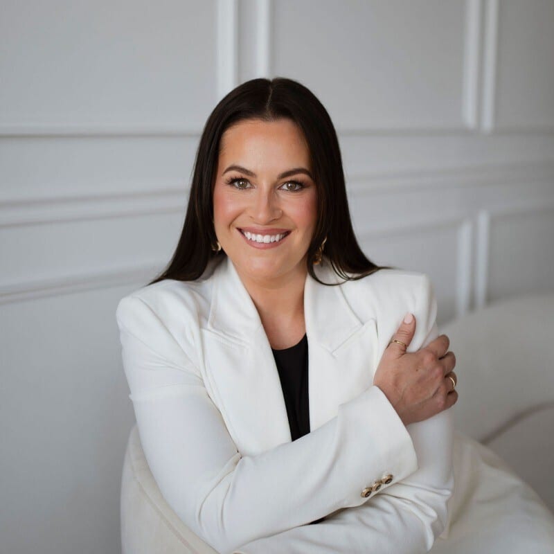 Smiling woman with dark hair in a white blazer and black top.