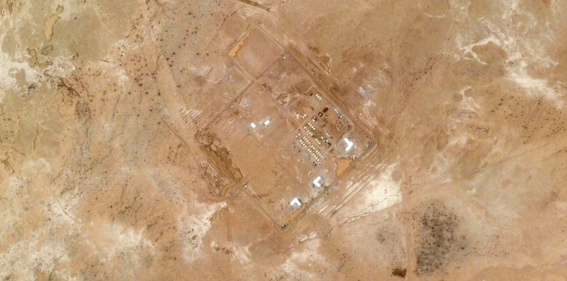 Satellite image of a desert facility with white buildings and many tents arranged in rows.