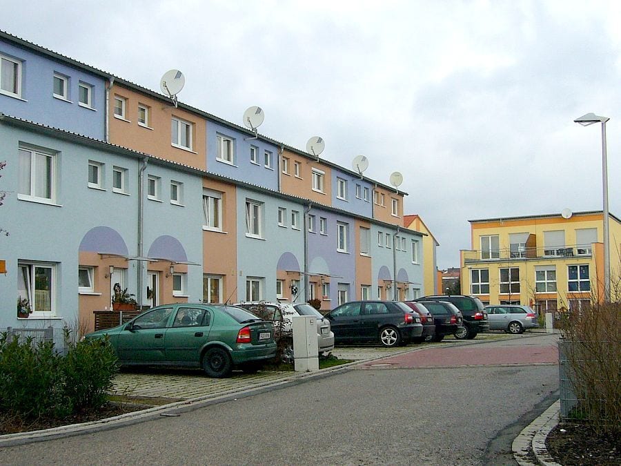 Colorful row houses, parked cars, and a yellow building under a gray sky.