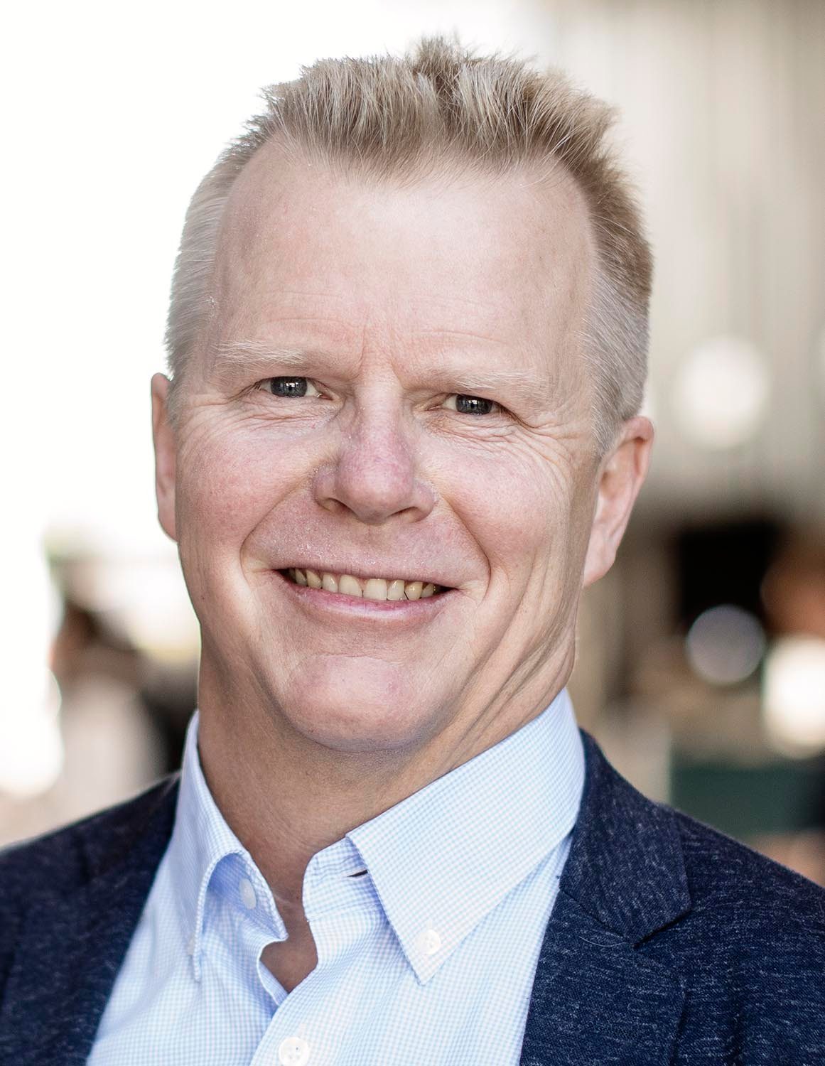 Smiling man's headshot: light hair, blue eyes, blue shirt, dark jacket.