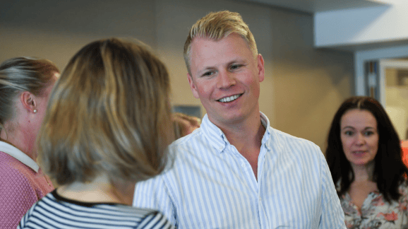 A smiling man in a striped shirt looks at a woman with her back to the camera.
