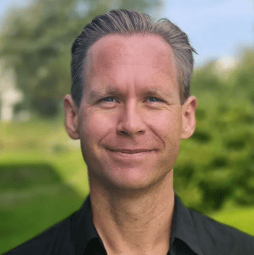 Smiling man with slicked-back gray hair in a black shirt, outdoors.