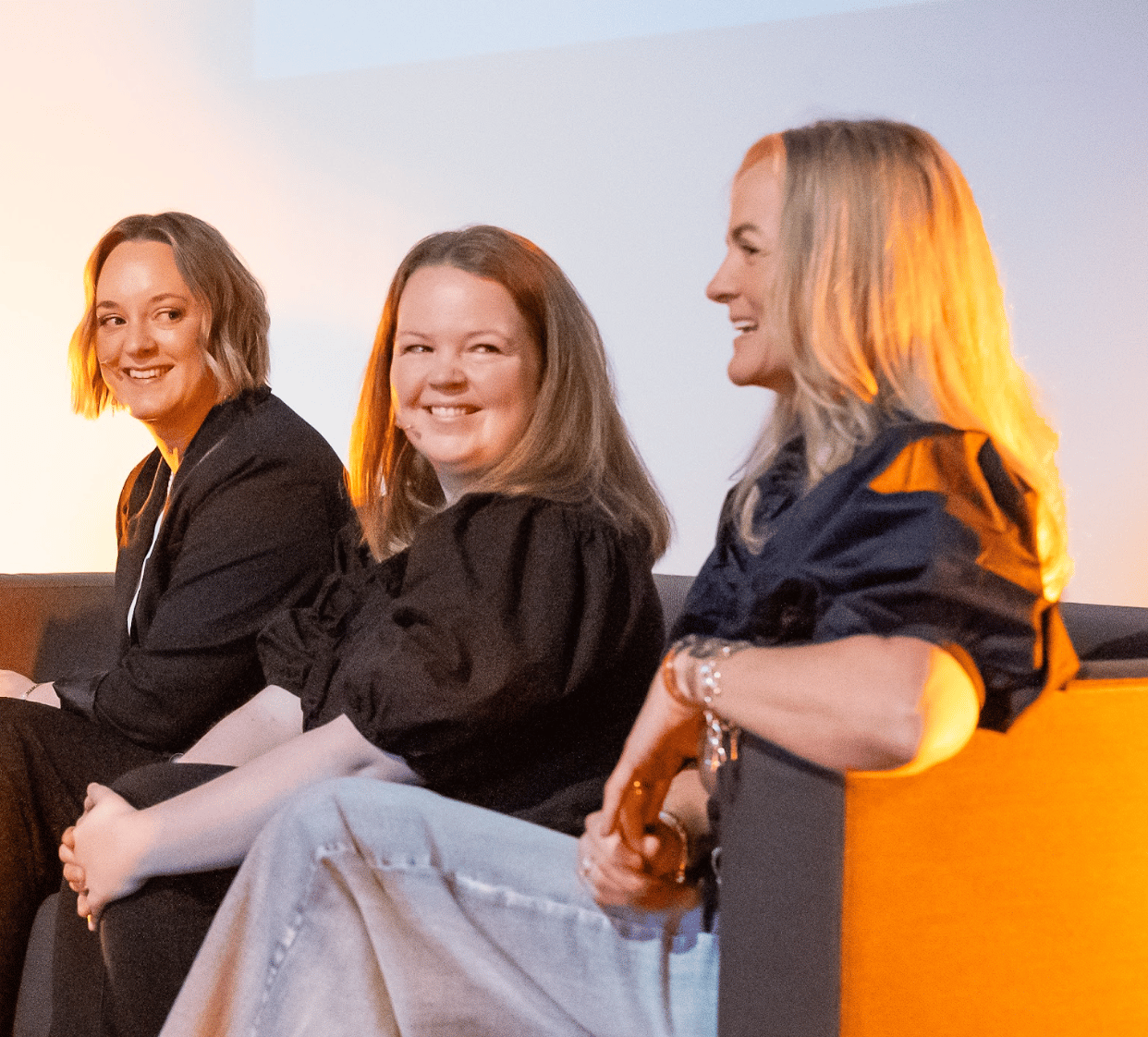 Three women sitting on a couch, smiling and talking.