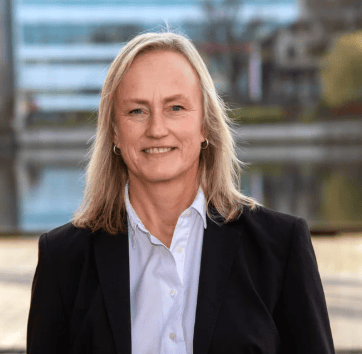 Smiling blonde woman in a white shirt and dark blazer.