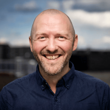 Headshot of a smiling bald man with a beard and blue shirt.