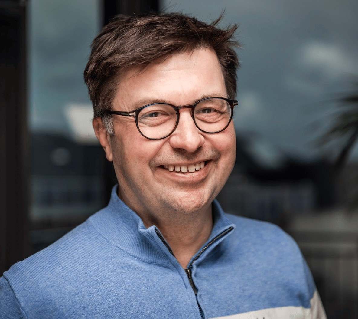Smiling man with glasses in a blue sweater.