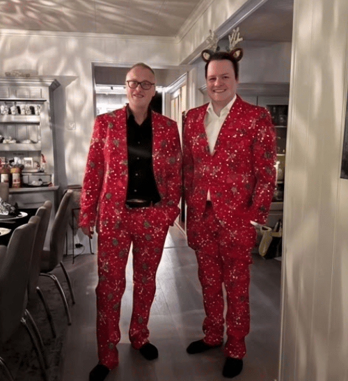 Two men in matching red Christmas suits, one with reindeer antlers.