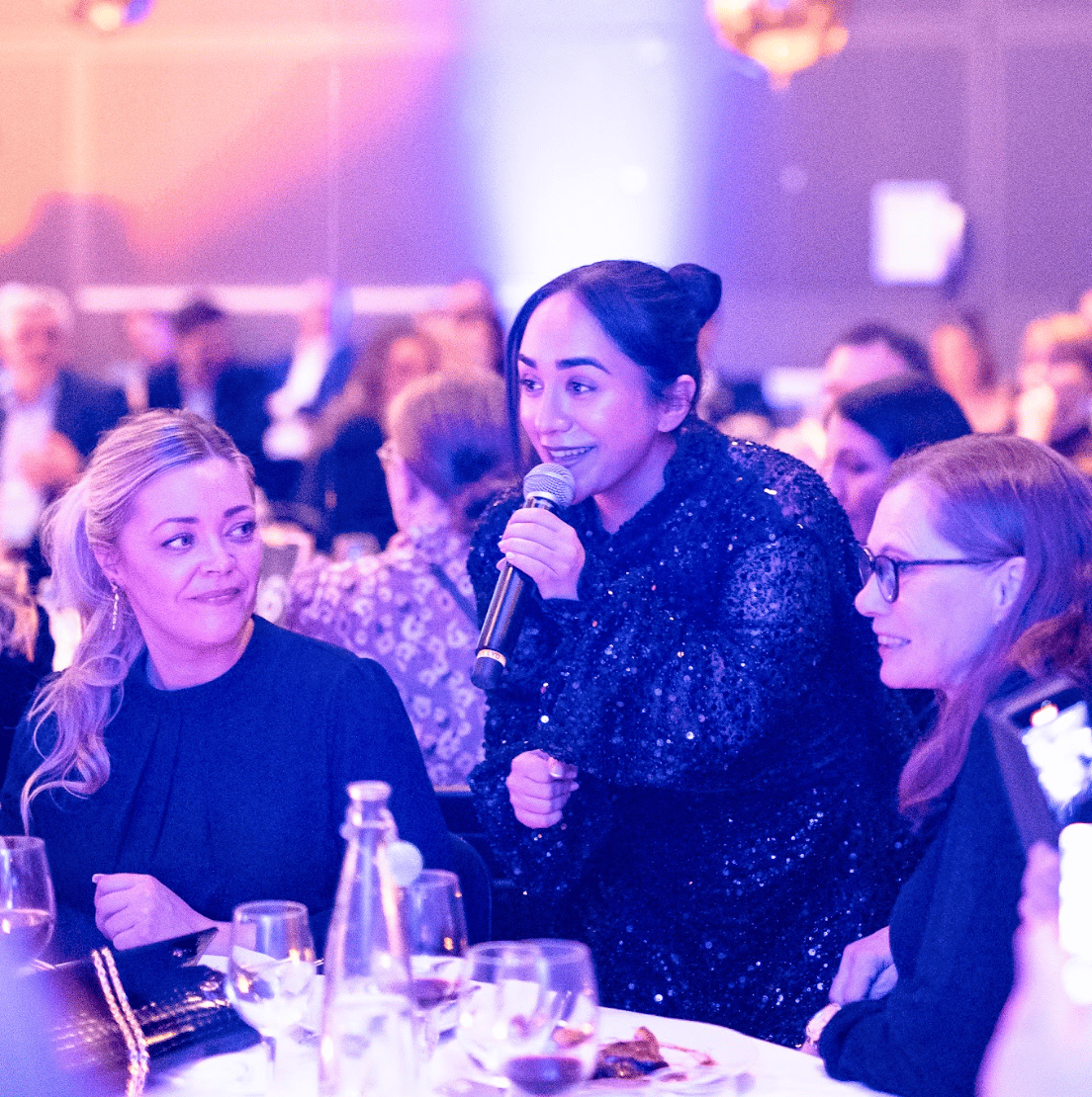 Speaker with microphone addressing guests at a formal dinner.