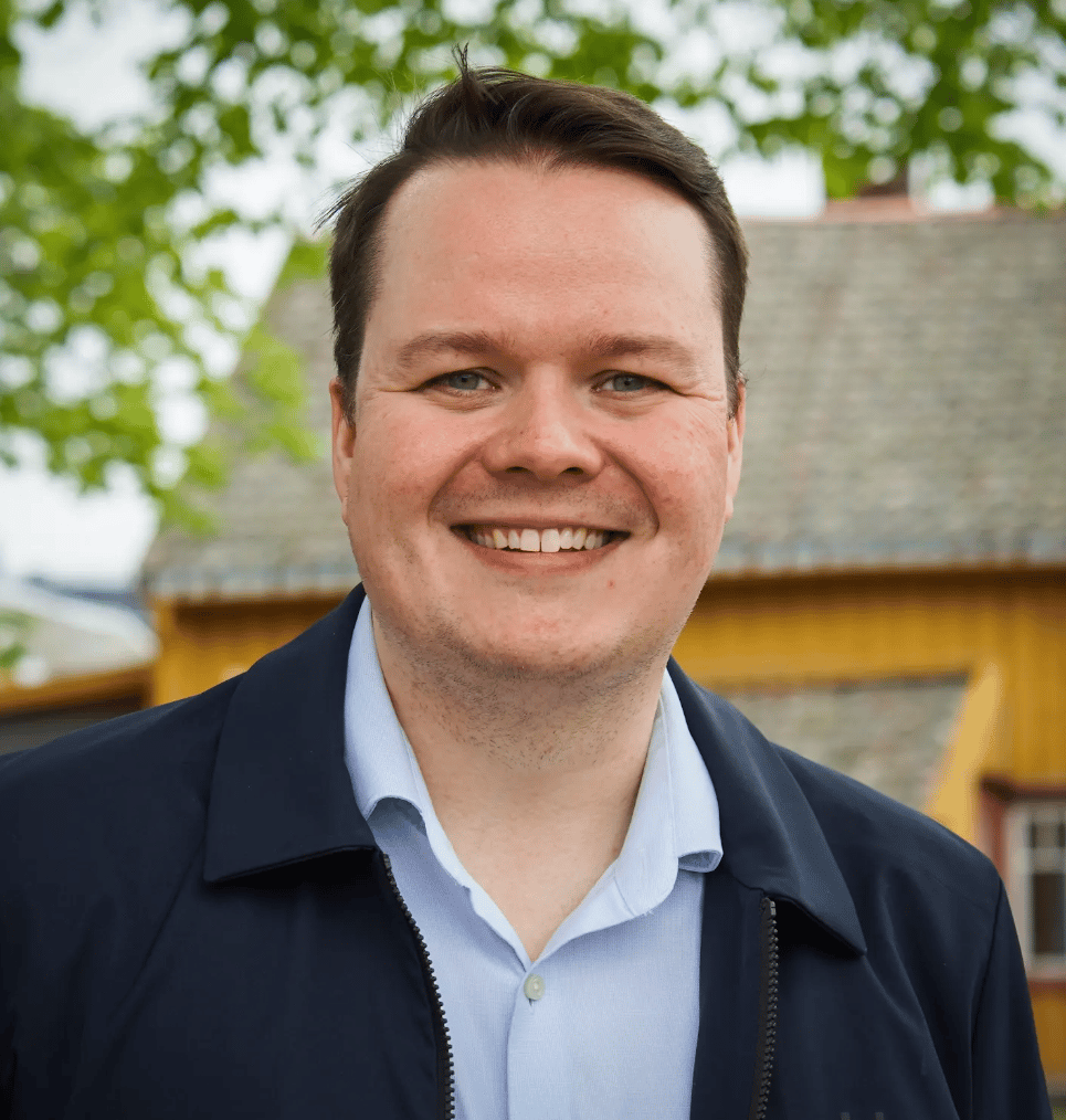 Smiling man in blue shirt and dark jacket.