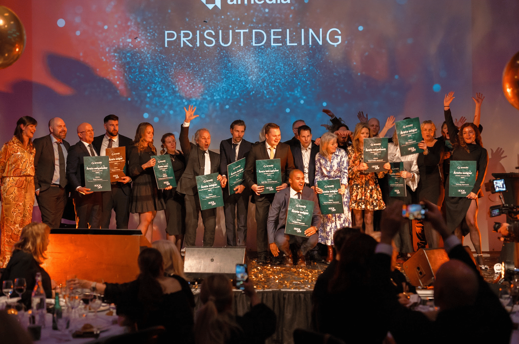 Group on stage celebrating an award ceremony, holding certificates and cheering.