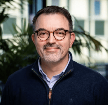 Smiling man with glasses and a blue sweater.