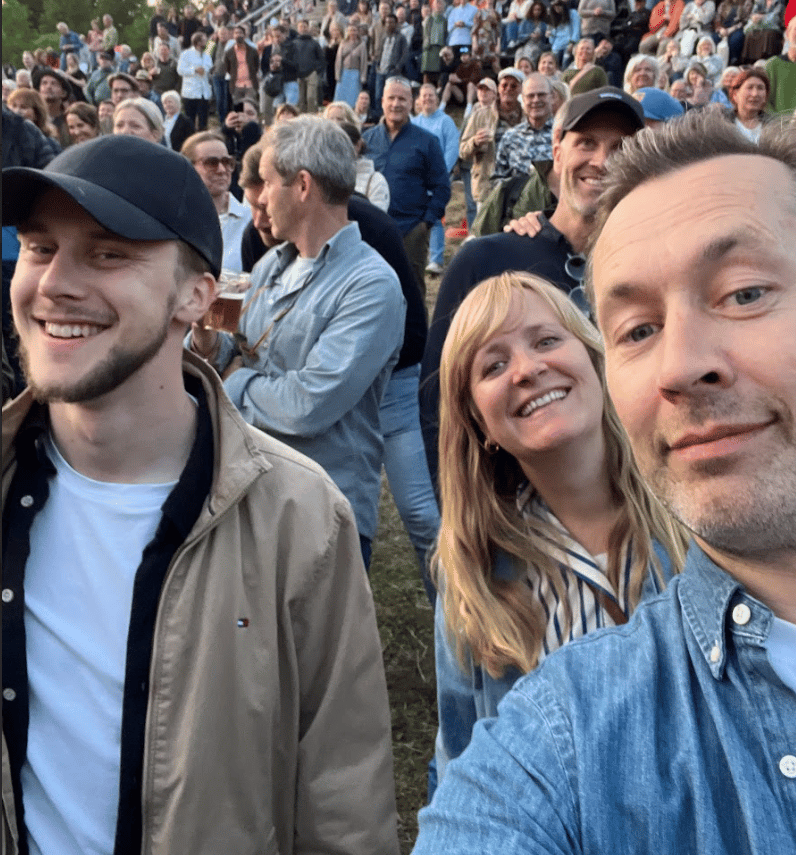 Smiling group taking a selfie at a crowded outdoor event.