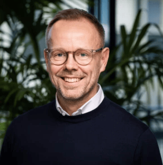 Headshot of a smiling man with glasses and a dark sweater.