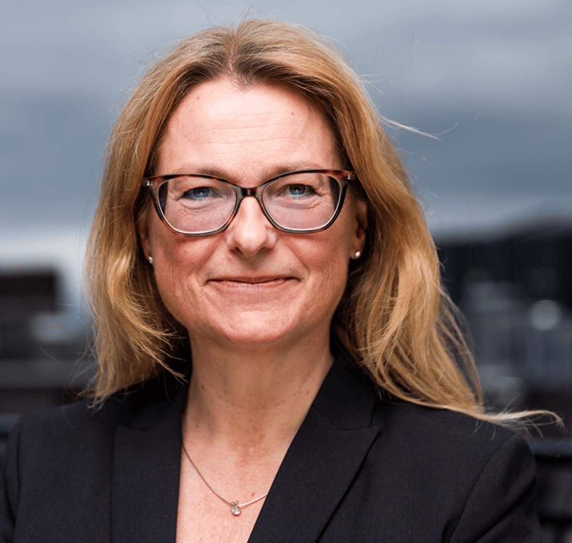 Smiling blonde woman with glasses in a black jacket, headshot.