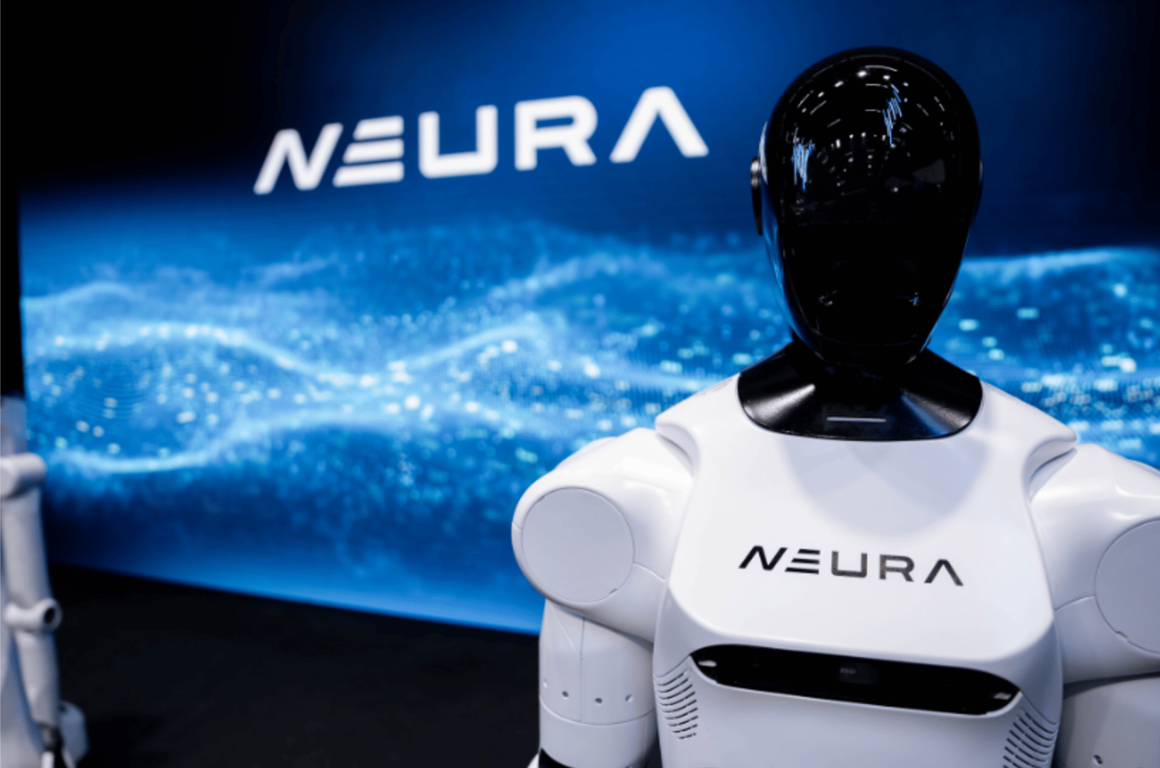 White humanoid robot with black head, 'NEURA' logo on chest and background screen.