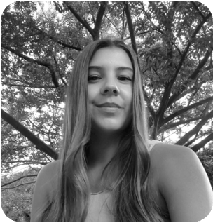 Black and white portrait of a young woman with long hair smiling, with trees in the background.