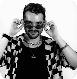 Black and white photo of a man adjusting his oval sunglasses, wearing a checkered shirt and chains.