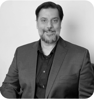 Black and white headshot of a smiling man with a beard, wearing a dark suit.