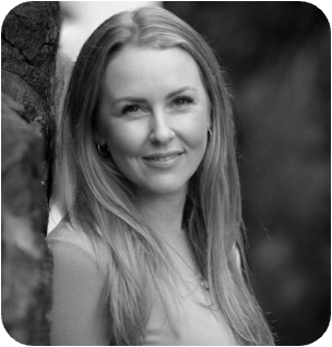 Black and white portrait of a smiling woman with long hair, leaning against a tree.