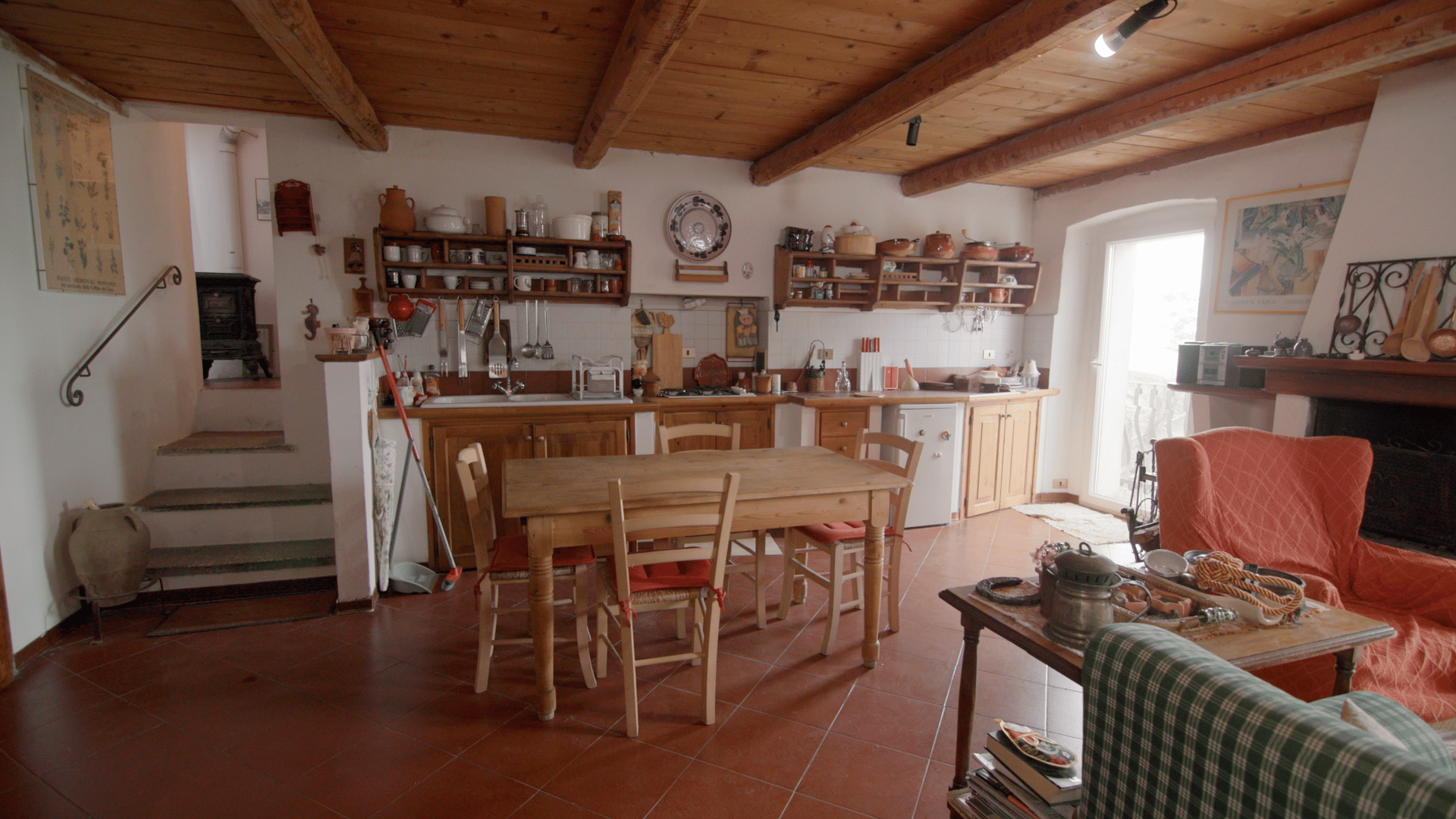 Cozy rustic open-plan kitchen, dining, and living area with wood beams and terracotta floors.